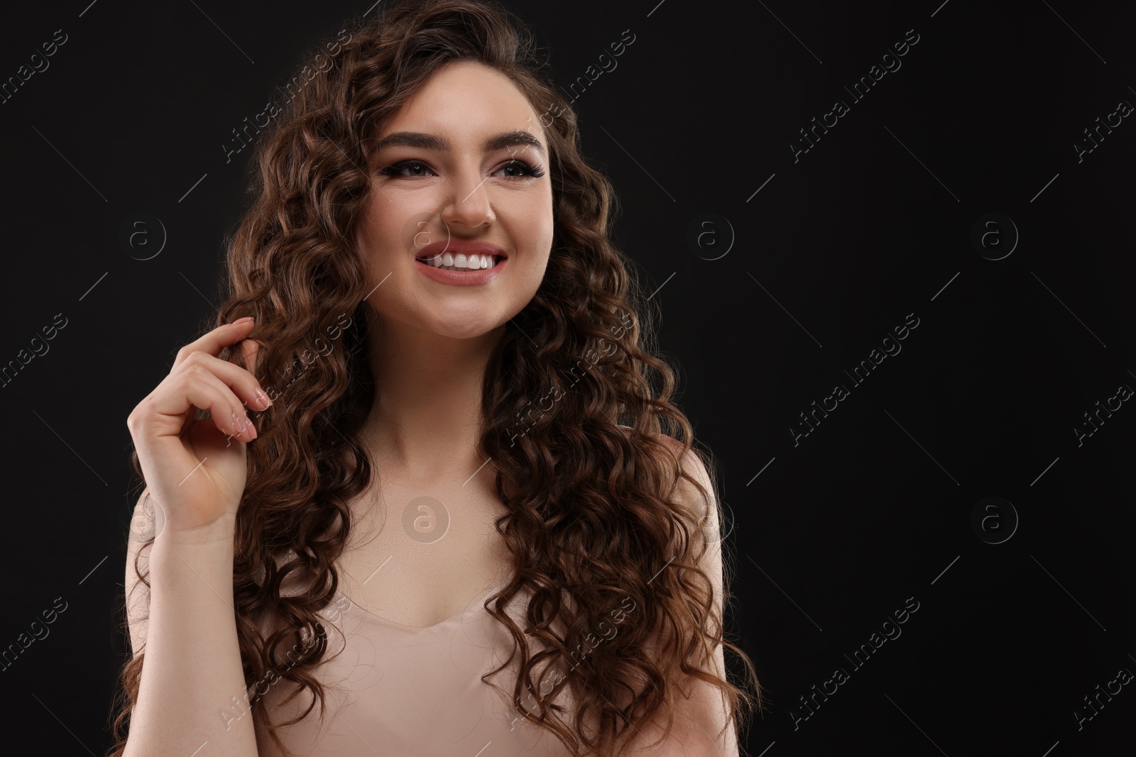 Photo of Beautiful young woman with long curly brown hair on black background, space for text