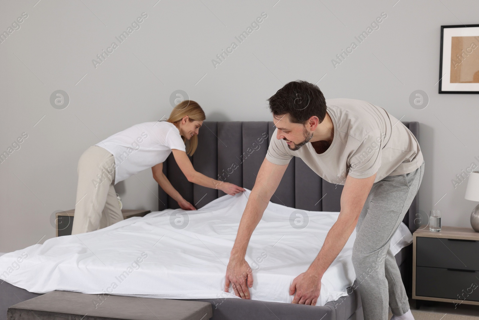 Photo of Couple changing bed linens in room. Domestic chores