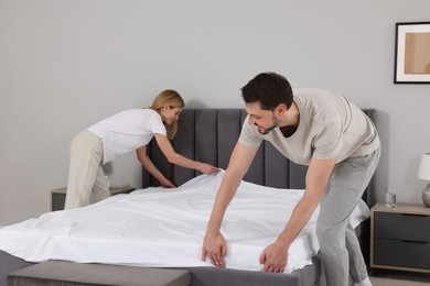 Photo of Couple changing bed linens in room. Domestic chores