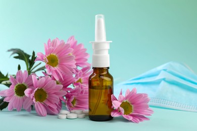 Photo of Allergy treatment. Nasal spray, pills and flowers on light blue background