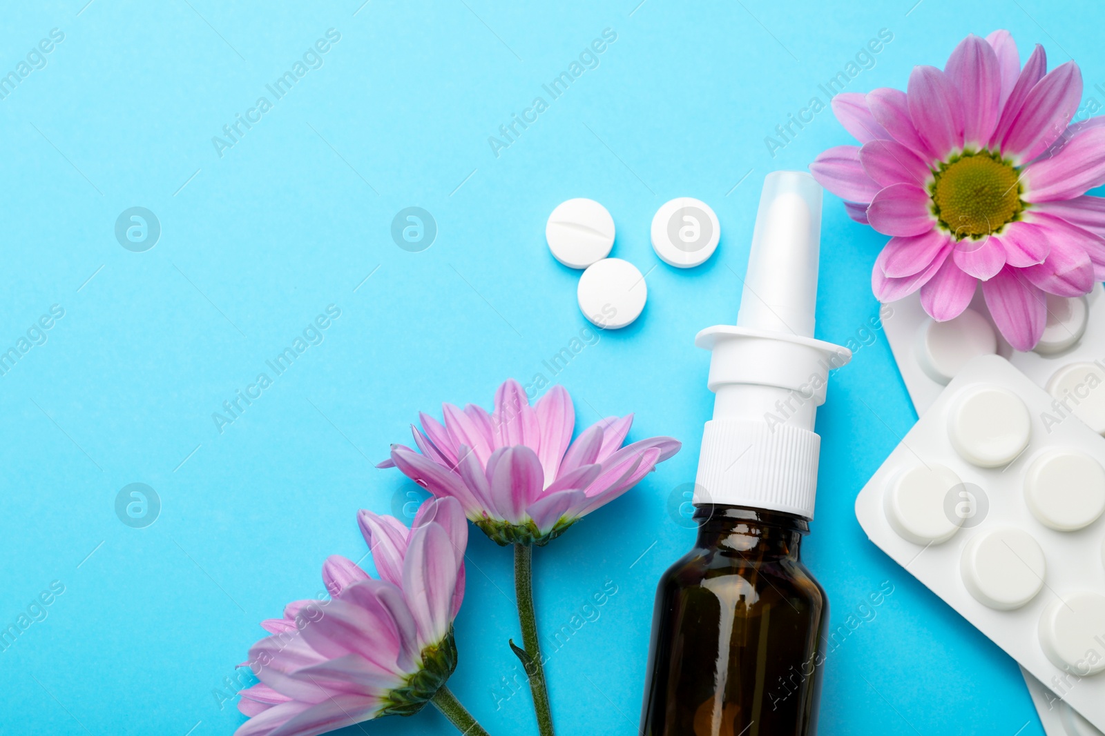 Photo of Allergy treatment. Nasal spray, pills and flowers on light blue background, flat lay