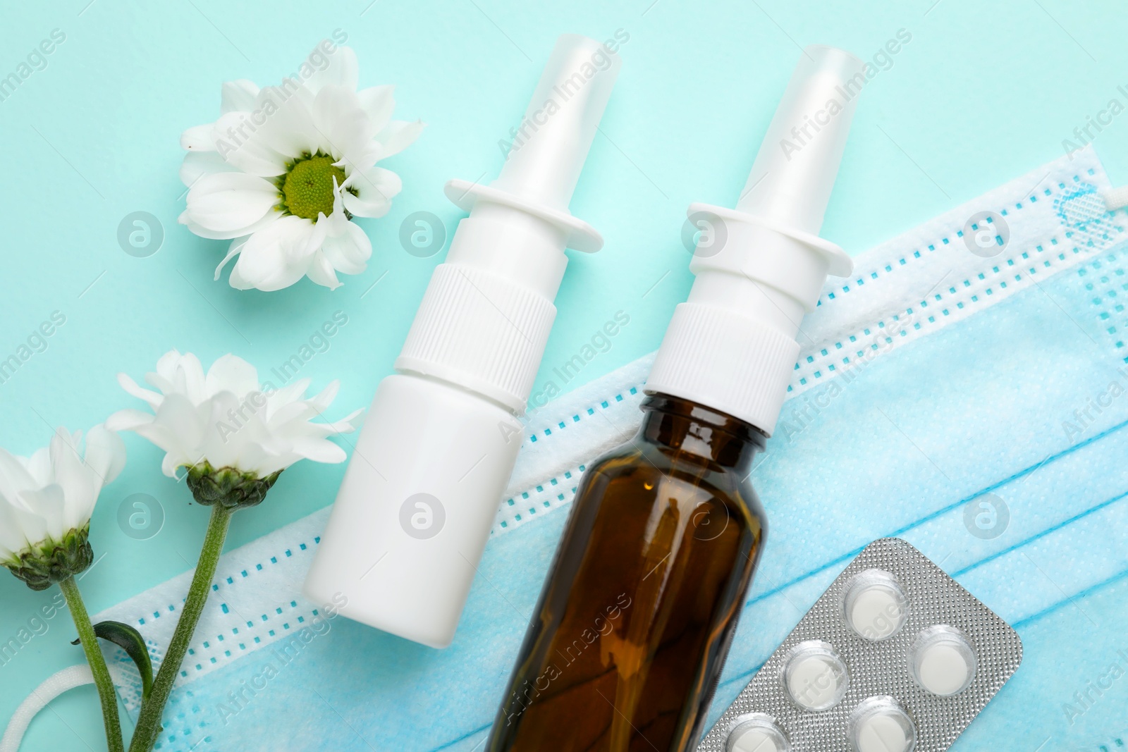 Photo of Allergy treatment. Different medications, protective mask and flowers on light blue background, flat lay