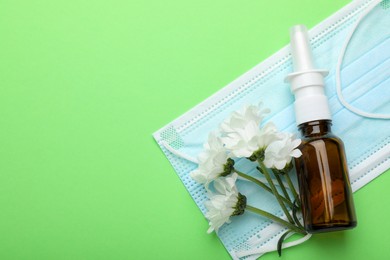 Photo of Allergy treatment. Nasal spray, protective mask and flowers on green background, top view. Space for text