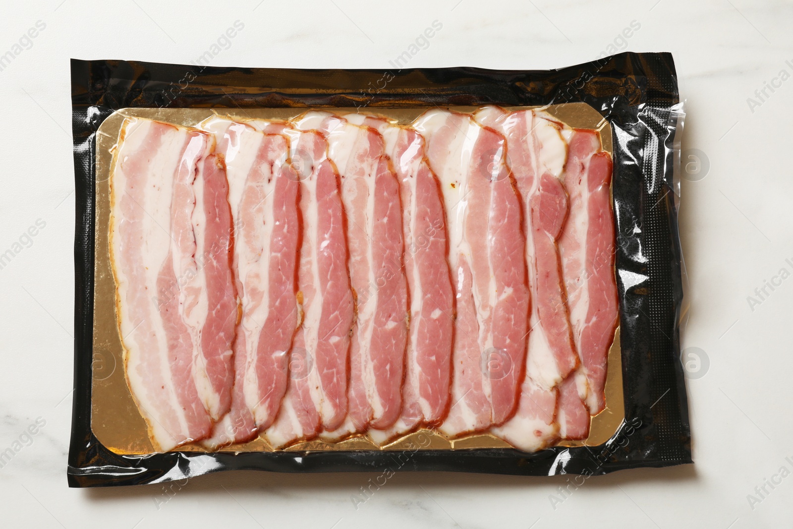 Photo of Pack of sliced bacon on white marble table, top view