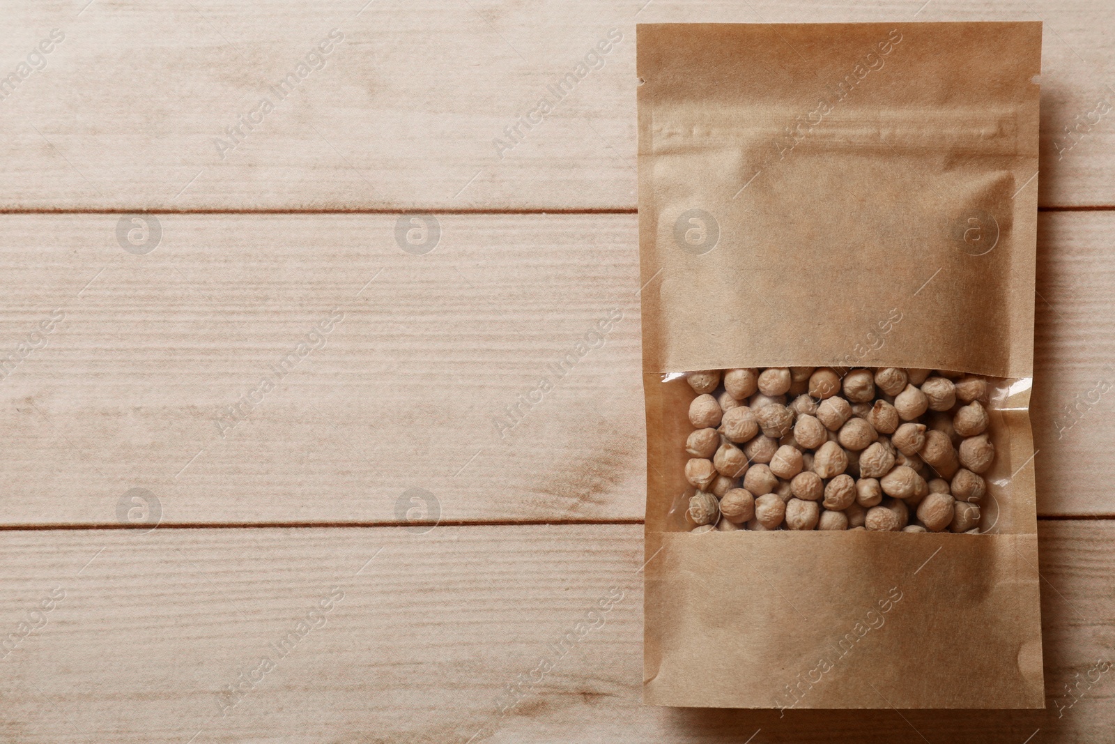 Photo of Paper pouch bag with chickpeas on wooden table, top view. Space for text