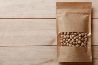 Photo of Paper pouch bag with chickpeas on wooden table, top view. Space for text