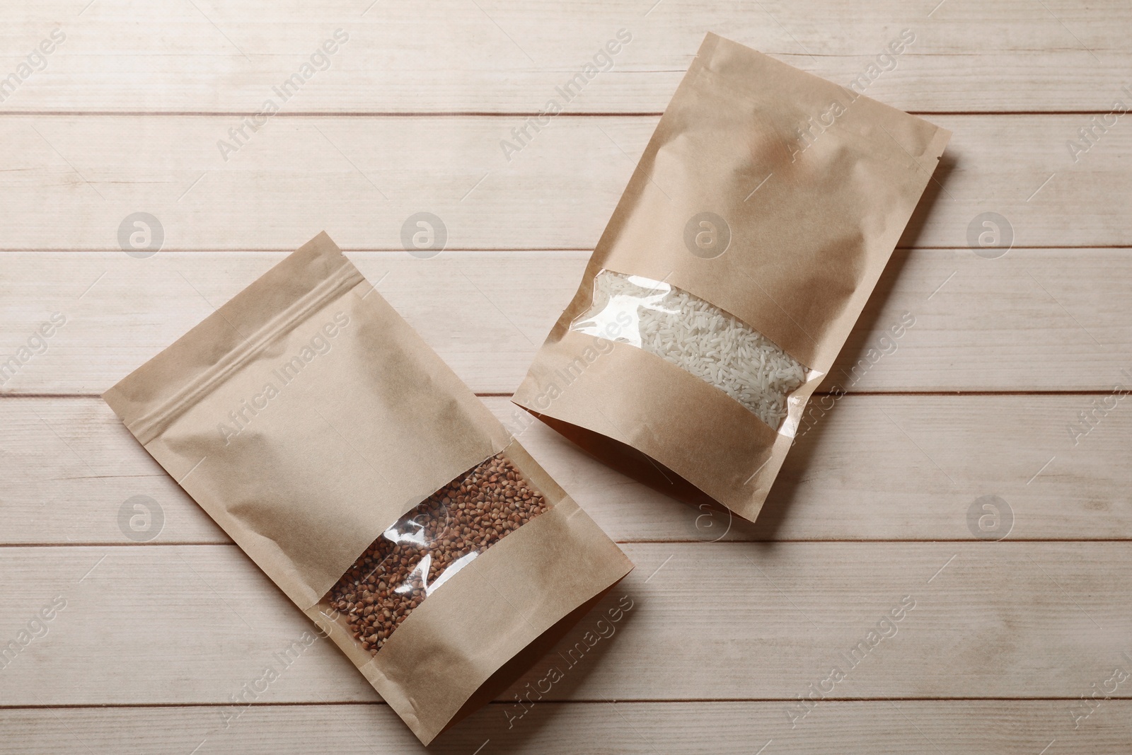 Photo of Paper pouch bags with buckwheat and rice on wooden table, top view