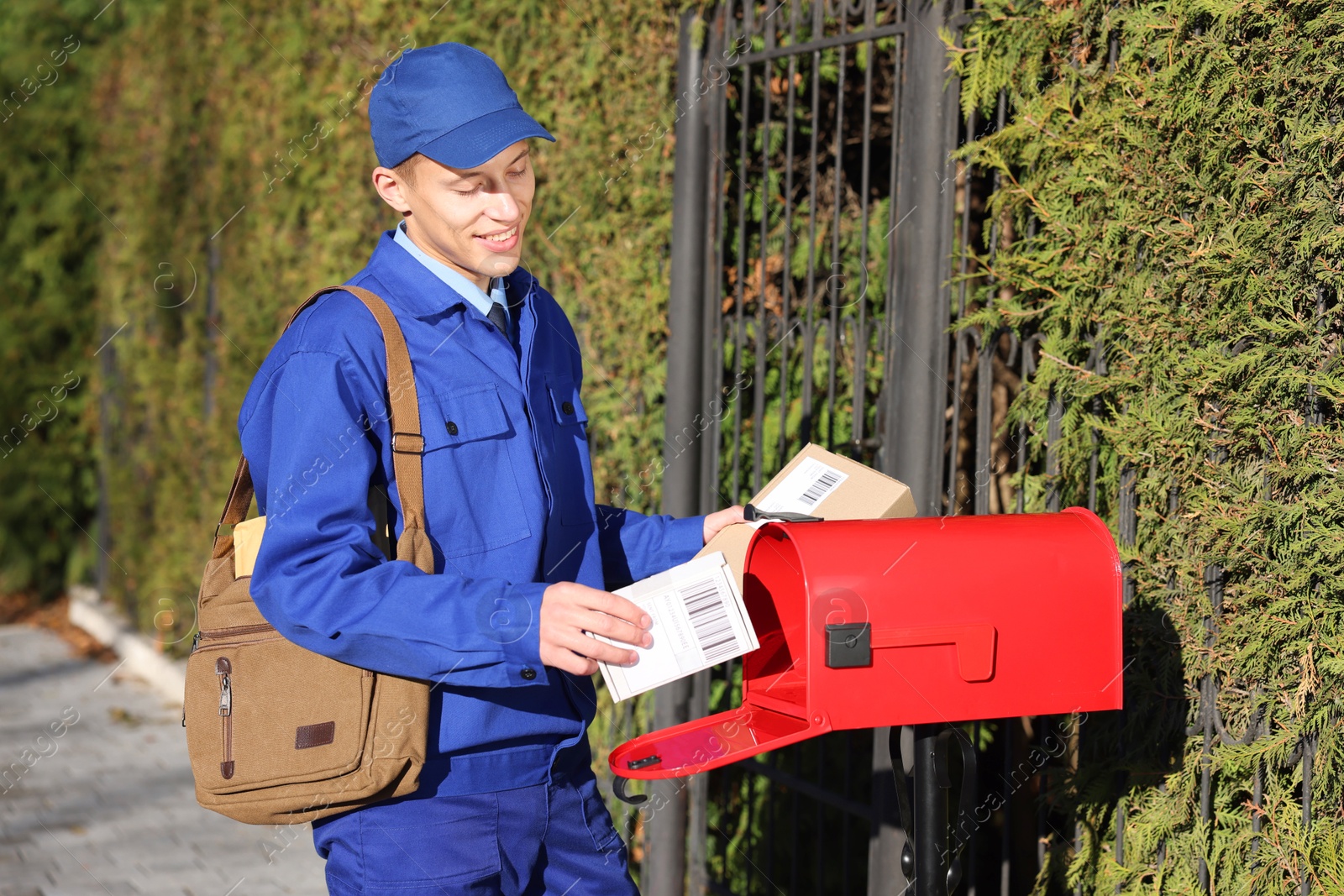 Photo of Postman putting parcel into mail box outdoors