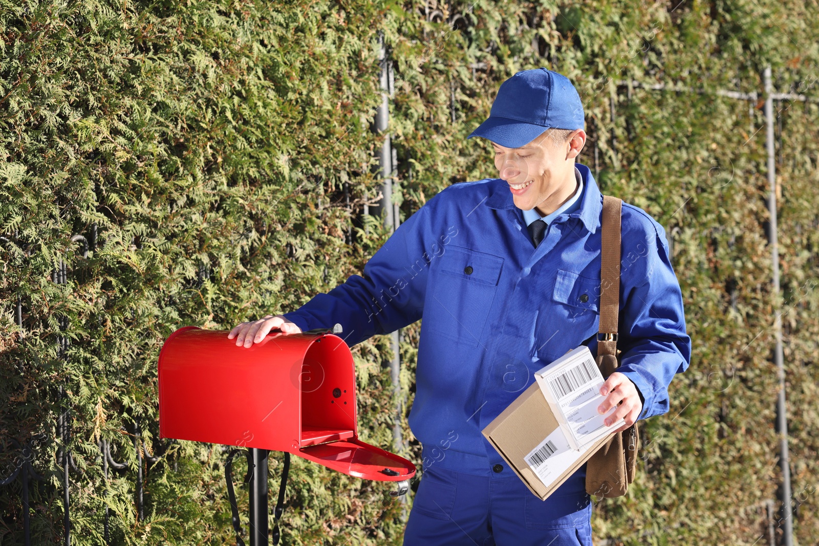 Photo of Postman putting parcel into mail box outdoors