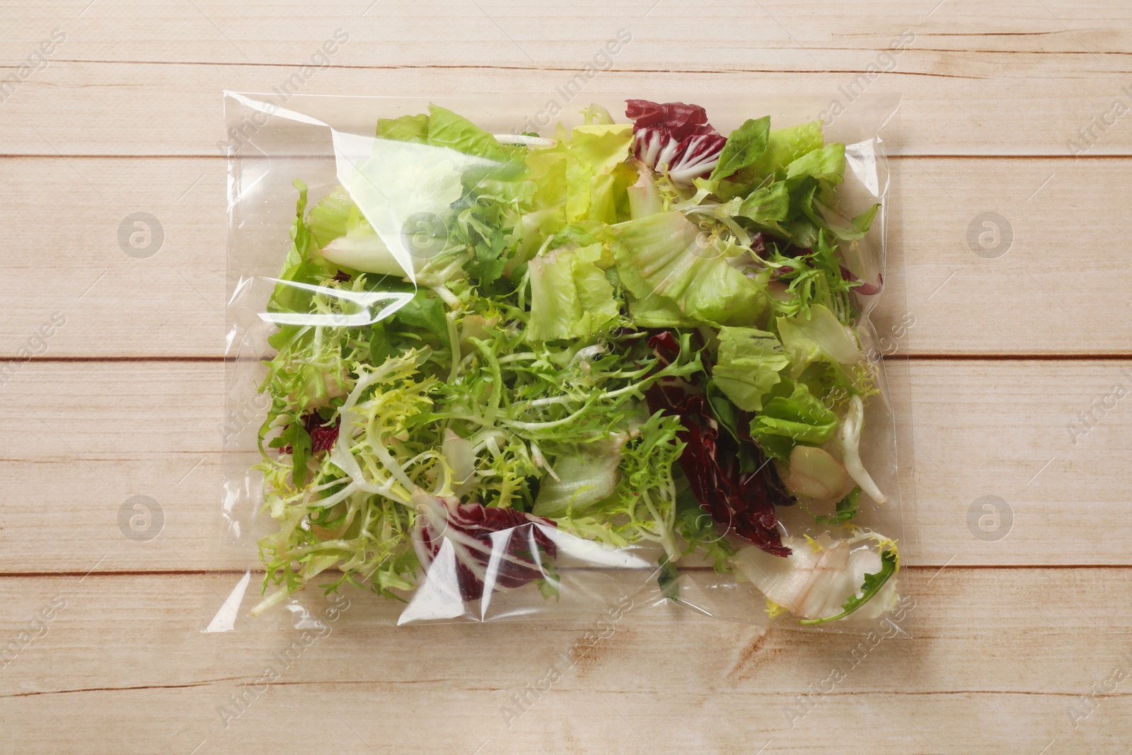 Photo of Pack of fresh salad mix on white wooden table, top view