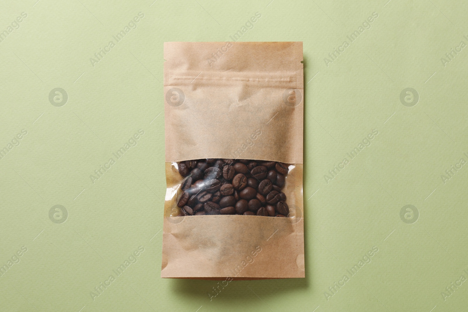 Photo of Paper pouch bag with coffee beans on green background, top view