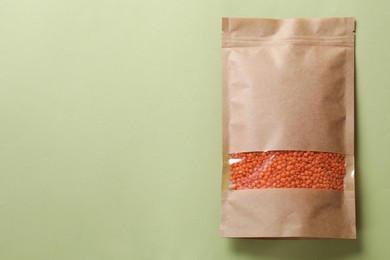 Photo of Paper pouch bag with lentil on green background, top view. Space for text