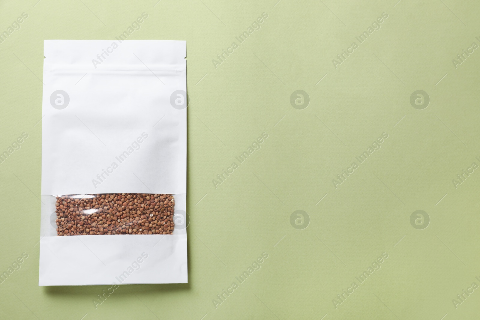 Photo of Paper pouch bag with buckwheat on green background, top view. Space for text