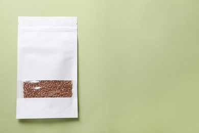 Photo of Paper pouch bag with buckwheat on green background, top view. Space for text