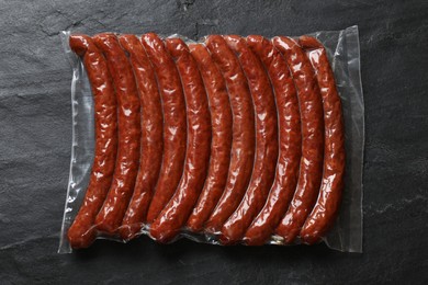 Photo of Pack of smoked sausages on black table, top view