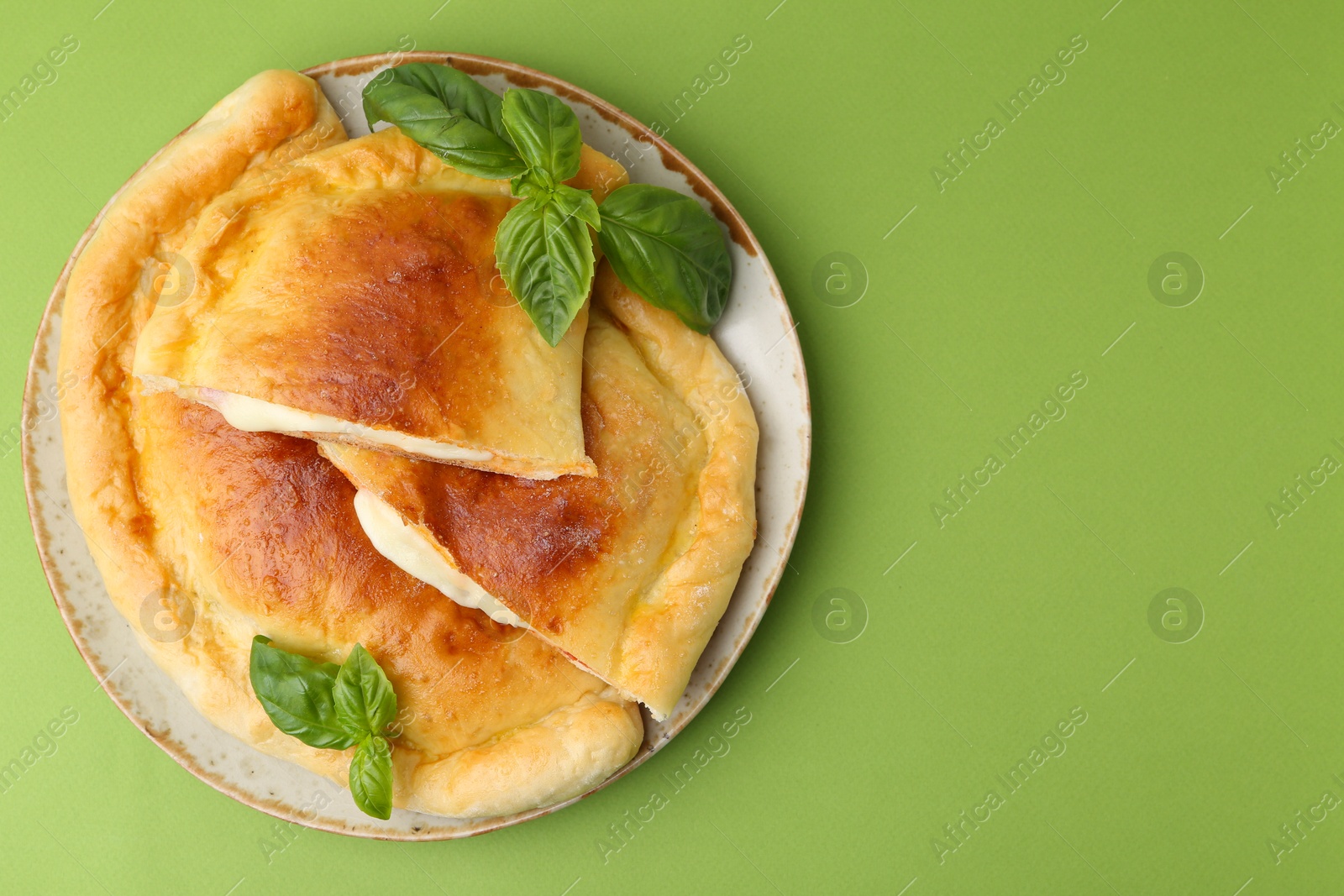 Photo of Pieces of delicious calzone pizza with mozzarella, tomatoes and basil on green background, top view. Space for text