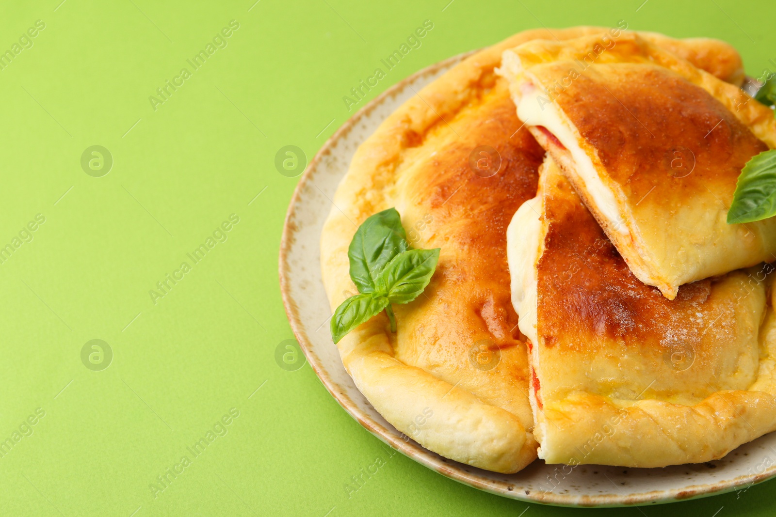 Photo of Pieces of delicious calzone pizza with mozzarella, tomatoes and basil on green background, closeup. Space for text