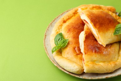 Photo of Pieces of delicious calzone pizza with mozzarella, tomatoes and basil on green background, closeup. Space for text