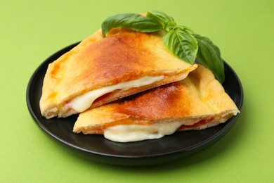 Photo of Pieces of delicious calzone pizza with mozzarella, tomatoes and basil on green background, closeup