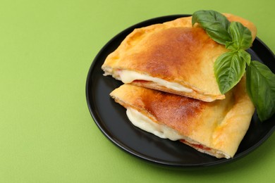 Photo of Pieces of delicious calzone pizza with mozzarella, tomatoes and basil on green background, closeup