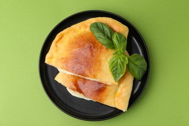 Photo of Pieces of delicious calzone pizza with mozzarella, tomatoes and basil on green background, top view