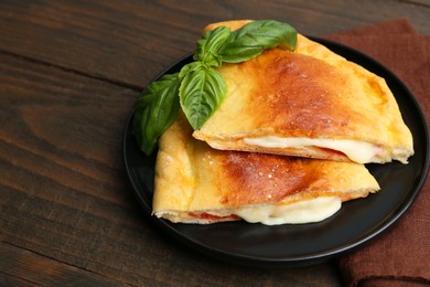 Photo of Pieces of delicious calzone pizza with mozzarella, tomatoes and basil on wooden table, closeup