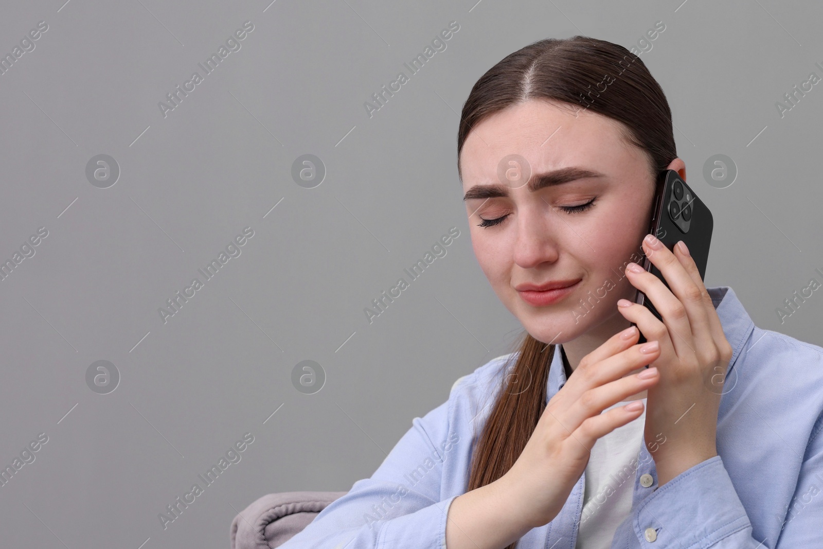 Photo of Stressed woman calling hotline for mental health help on grey background. Space for text