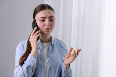 Photo of Stressed woman calling hotline for mental health help near window at home. Space for text