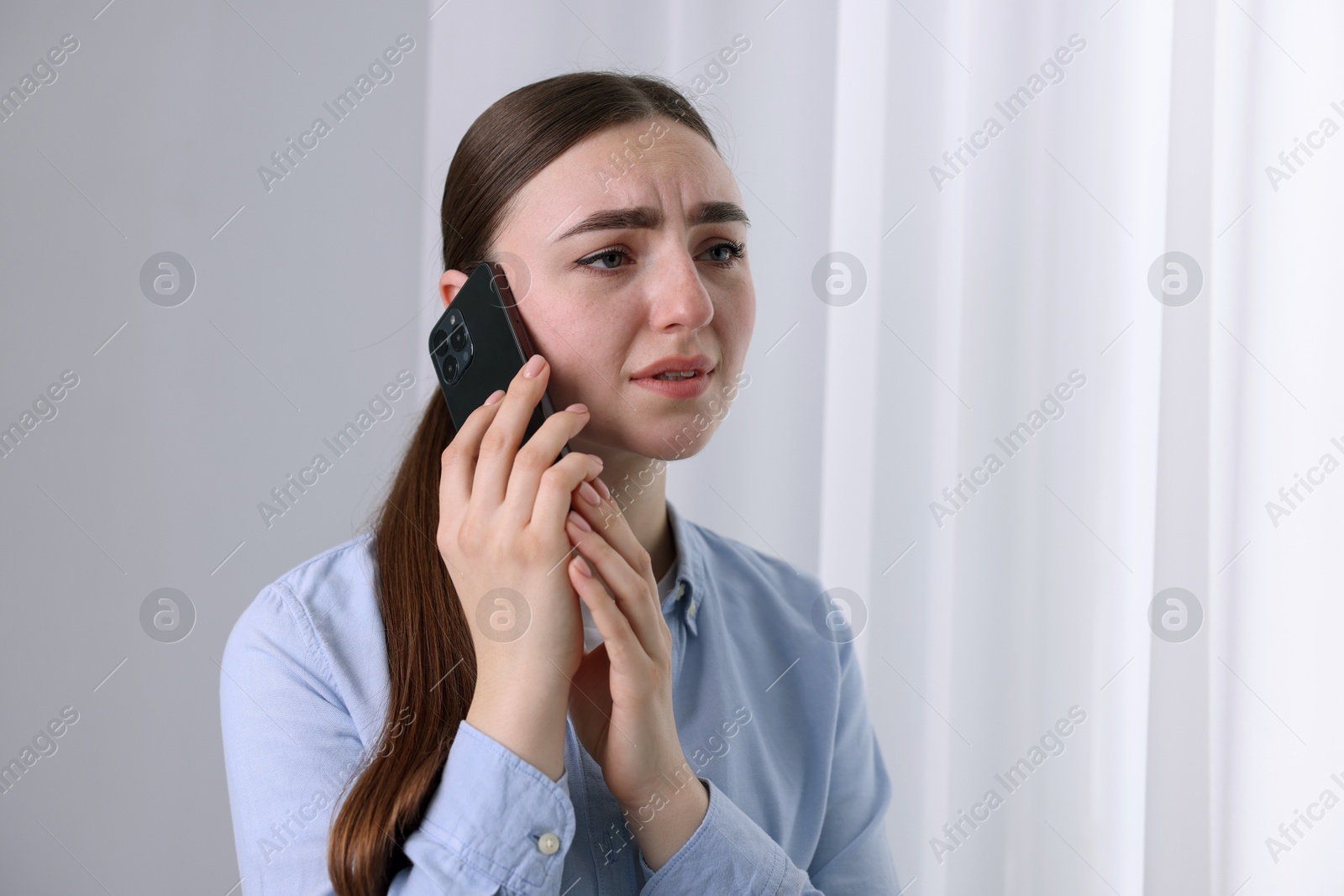 Photo of Stressed woman calling hotline for mental health help near window at home. Space for text