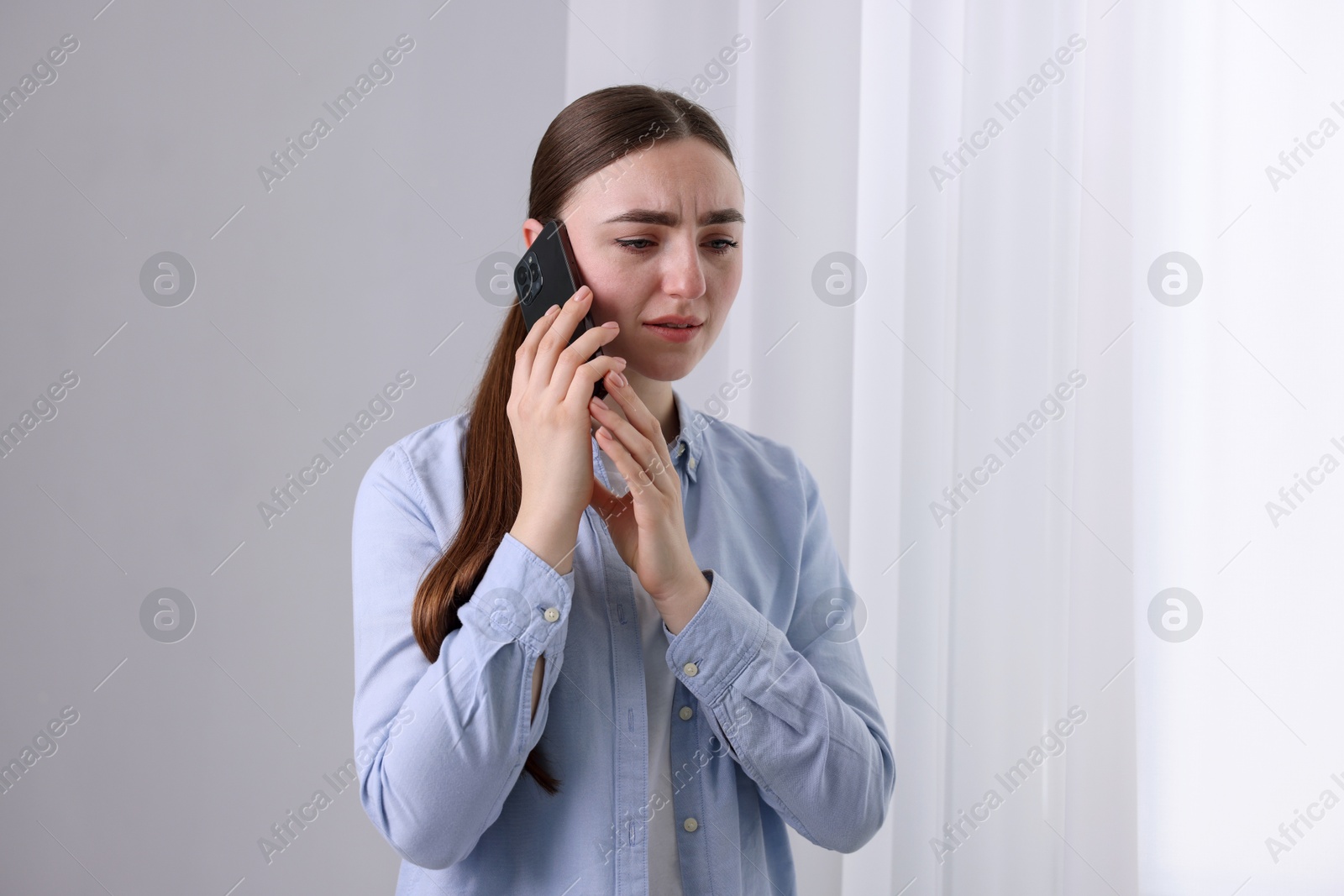 Photo of Stressed woman calling hotline for mental health help near window at home. Space for text