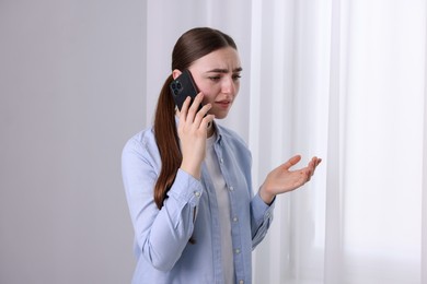 Photo of Stressed woman calling hotline for mental health help near window at home