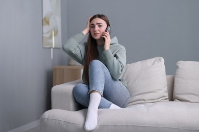 Photo of Depressed woman calling hotline for mental health help on sofa at home