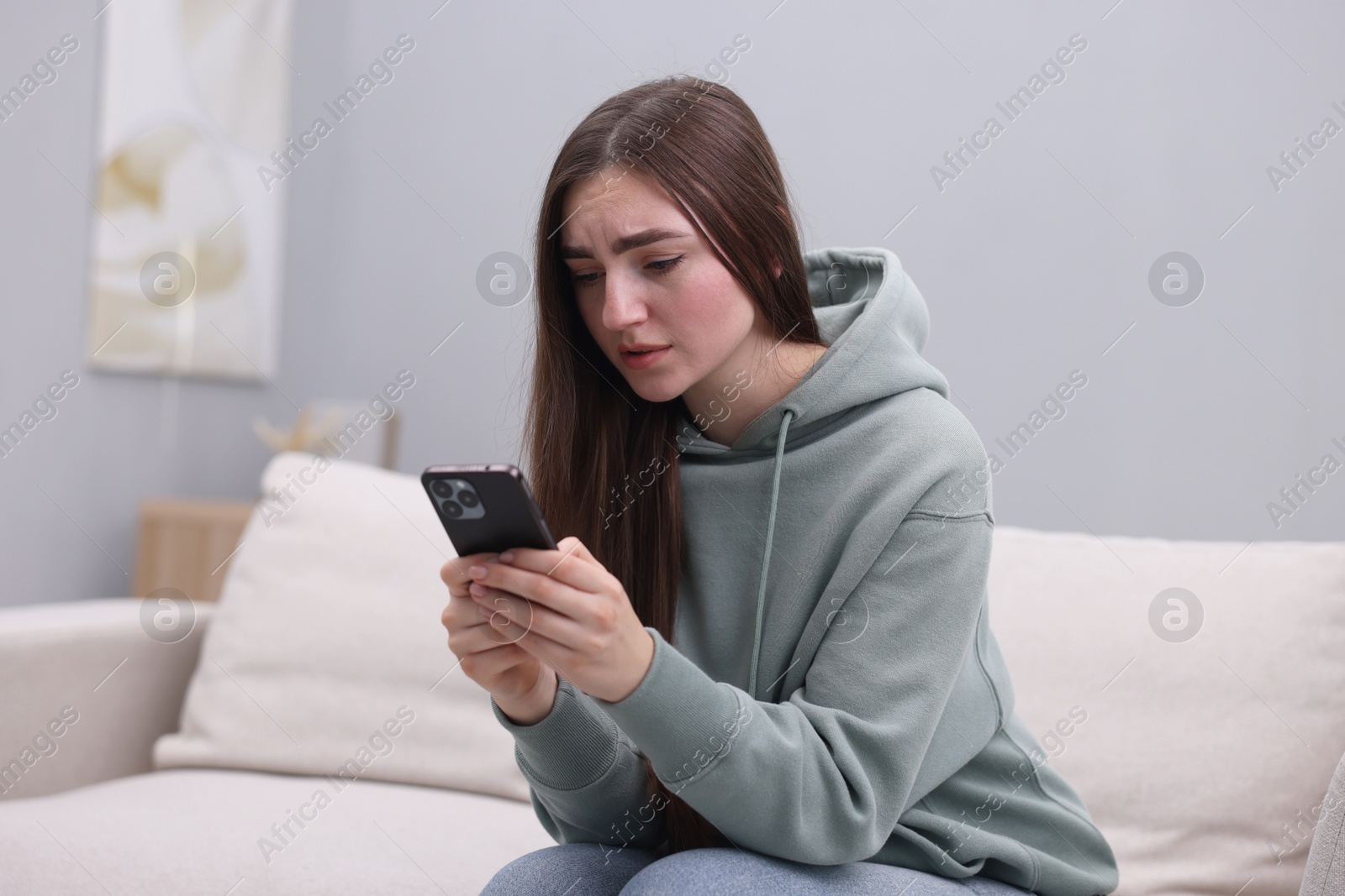 Photo of Depressed woman calling hotline for mental health help on sofa at home