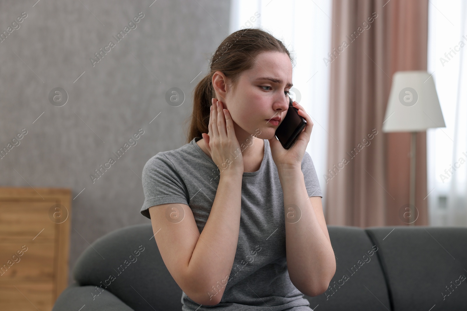 Photo of Depressed woman calling hotline for mental health help on sofa at home