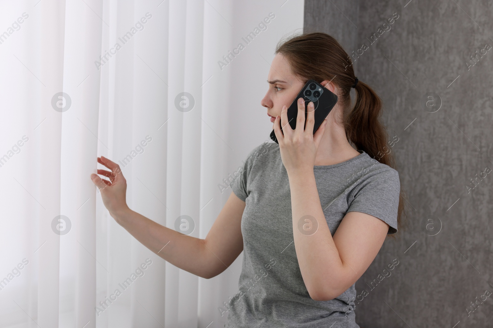 Photo of Stressed woman calling hotline for mental health help near window at home