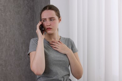 Photo of Stressed woman calling hotline for mental health help near window at home. Space for text