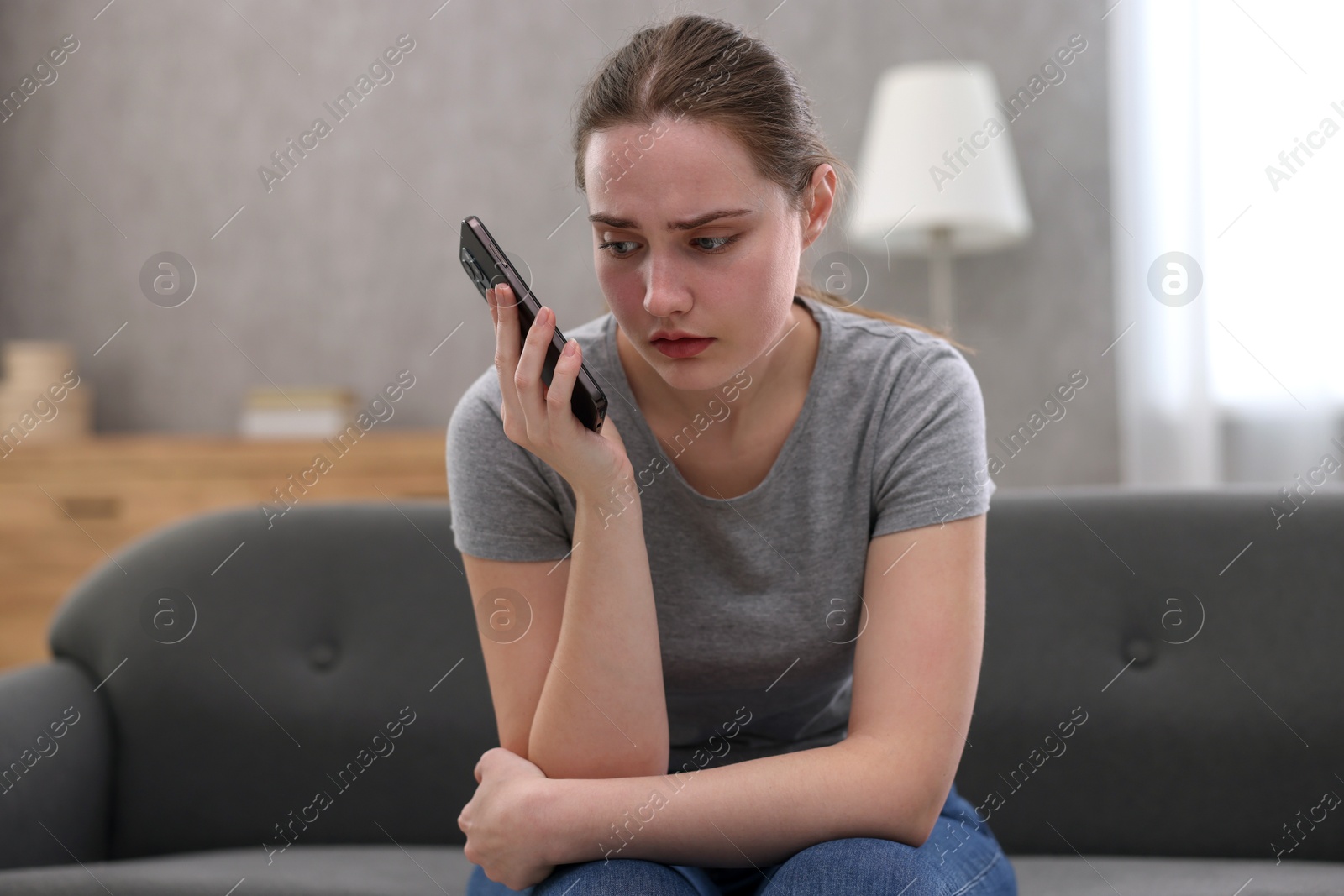 Photo of Depressed woman calling hotline for mental health help on sofa at home