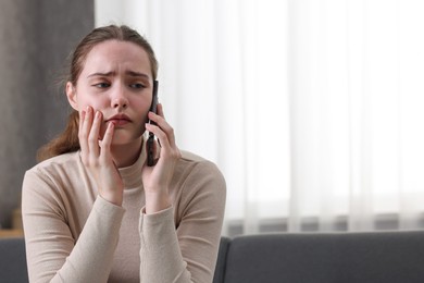 Photo of Depressed woman calling hotline for mental health help on sofa at home. Space for text