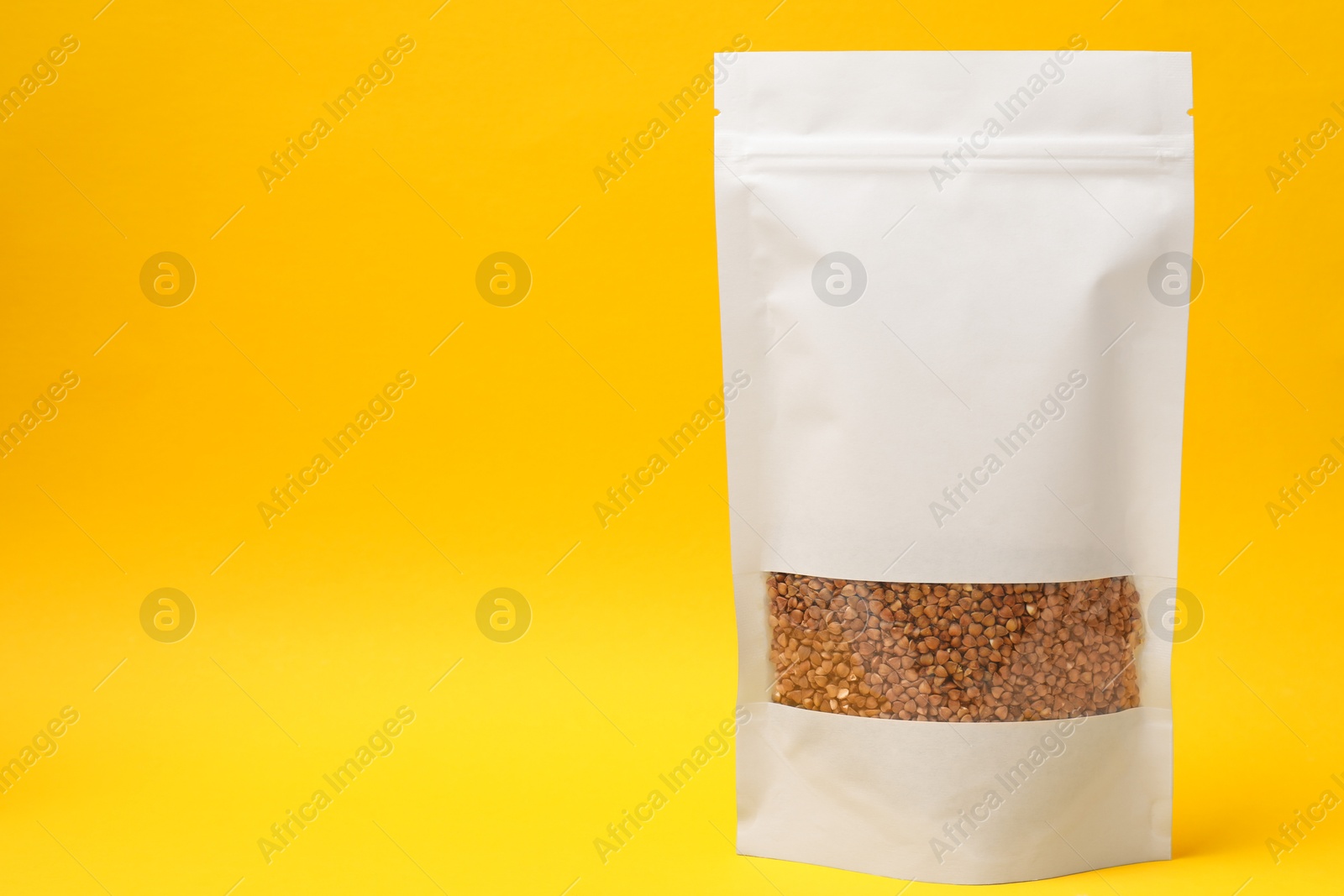 Photo of Paper pouch bag with buckwheat on yellow background, space for text