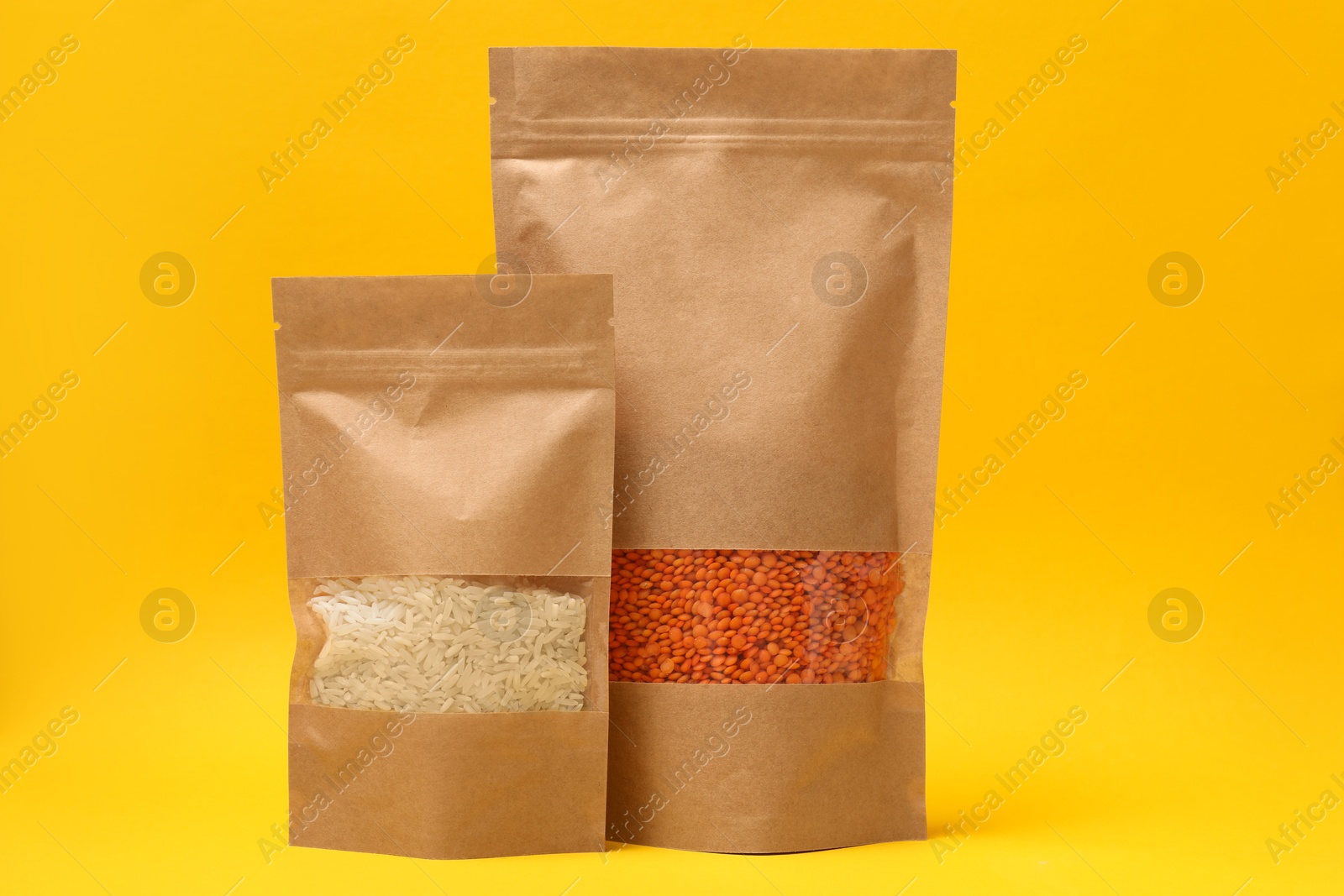 Photo of Paper pouch bags with lentil and rice on yellow background