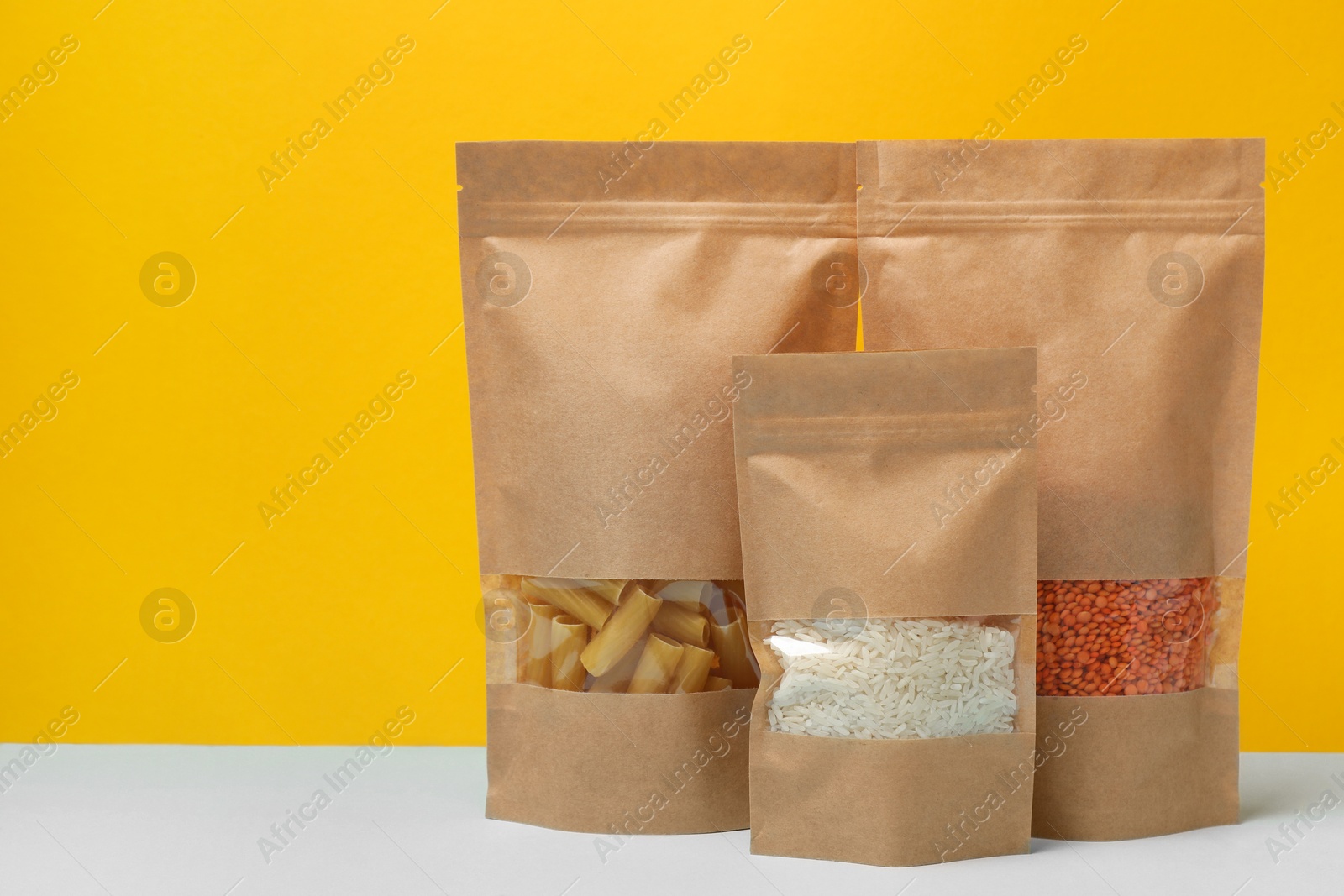 Photo of Paper pouch bags with different products on table against yellow background, space for text