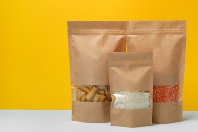 Photo of Paper pouch bags with different products on table against yellow background, space for text