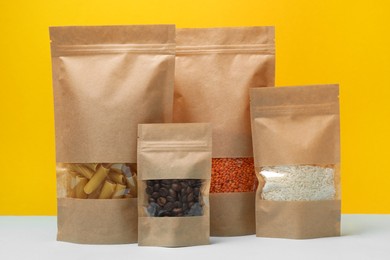 Photo of Paper pouch bags with different products on table against yellow background