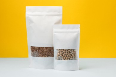 Photo of Paper pouch bags with chickpeas and buckwheat on table against yellow background