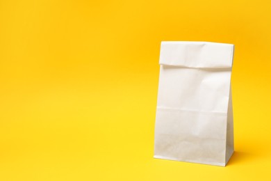 Photo of One closed paper bag on yellow background, space for text