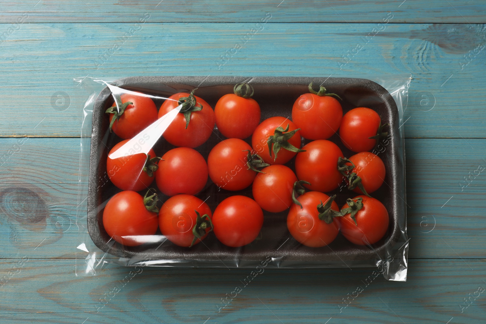 Photo of Pack of fresh tomatoes on light blue wooden table, top view