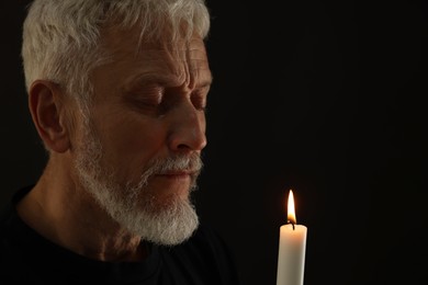 Photo of Sad senior man with burning candle crying on black background. Grieving loss