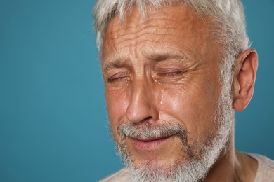 Photo of Sad senior man crying on light blue background, closeup. Space for text