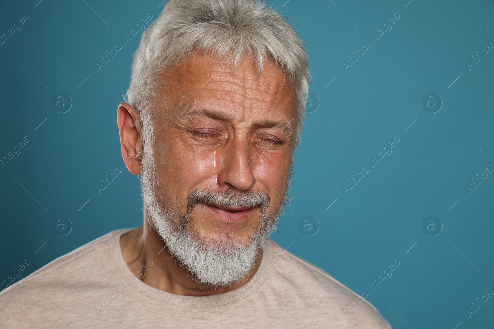 Photo of Sad senior man crying on light blue background, space for text