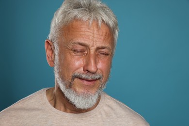 Photo of Sad senior man crying on light blue background, space for text